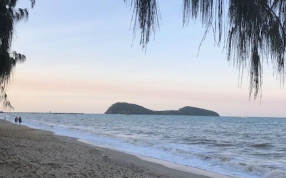 Looking along a beach, an island visible close by.