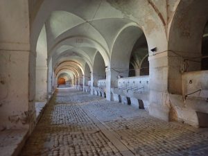 Looking down a very long hall with gothic arched ceiling and, along one side, what looks like feeding troughs also carved from stone.