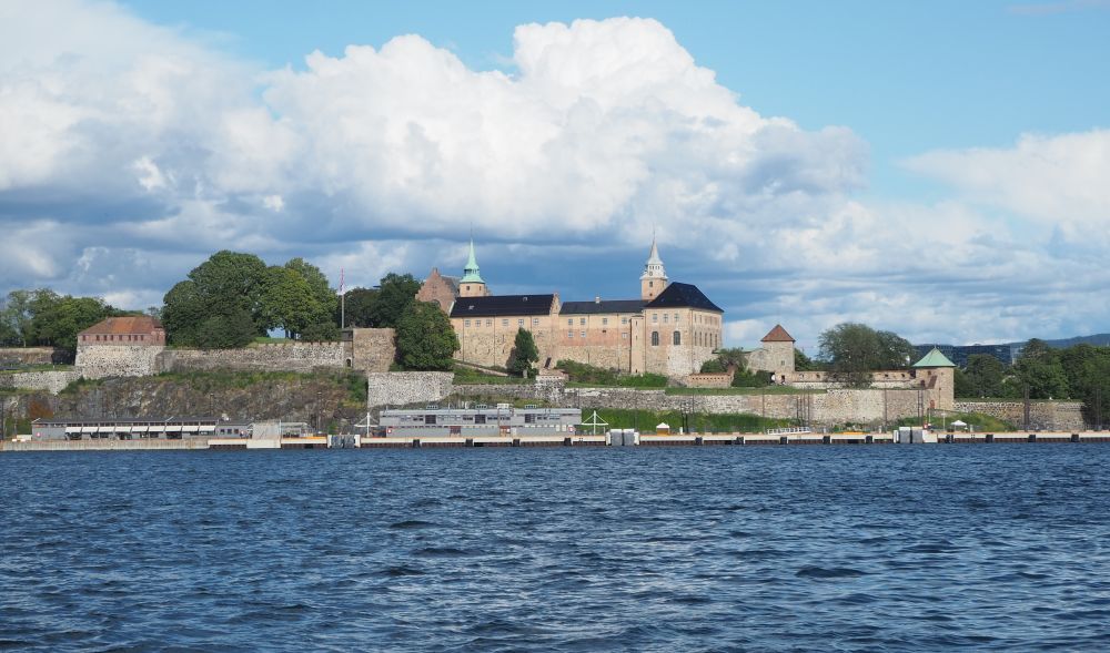 Walls and a larger building inside them on a low outcropping of rock on the water.