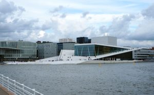 Seen across water, the building has a central square structure of glass with long, slanted sections around it and up its sides.