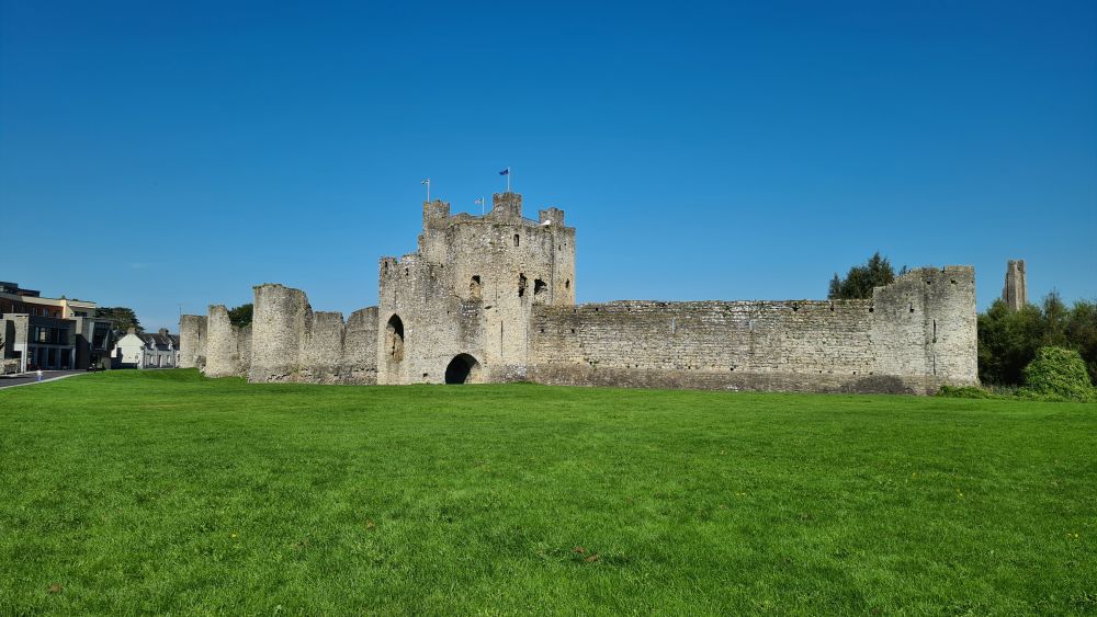 A long wall, with stone guard towers here and there, and a larger stone building behind it.