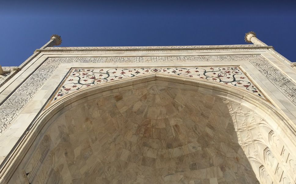 Looking up at a white marble arch with detailed floral and calligraphic inlays.