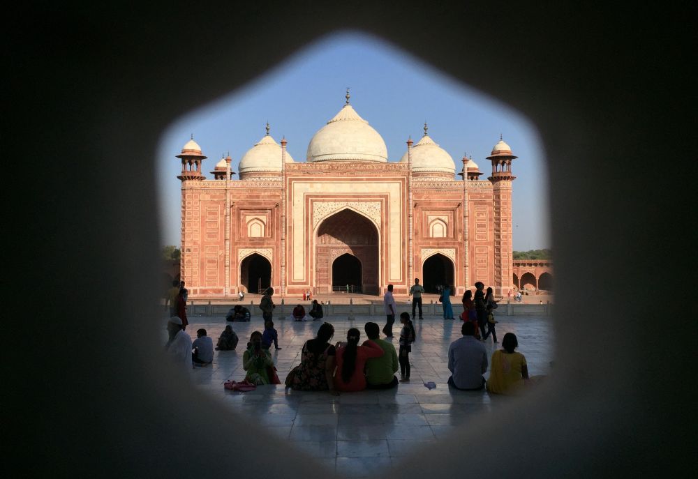 Looking through a six-sided opening toward the red stone mosque with domes and small towers at the corners.