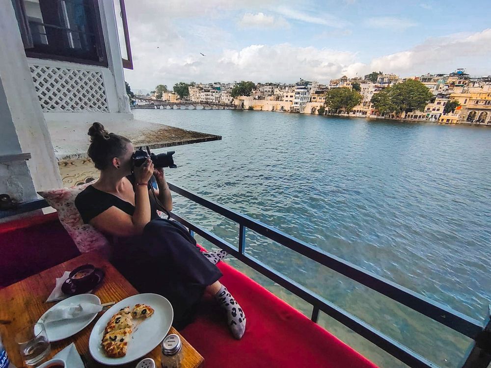 Woman with camera on the balcony of a ship with a tray of food beside her.