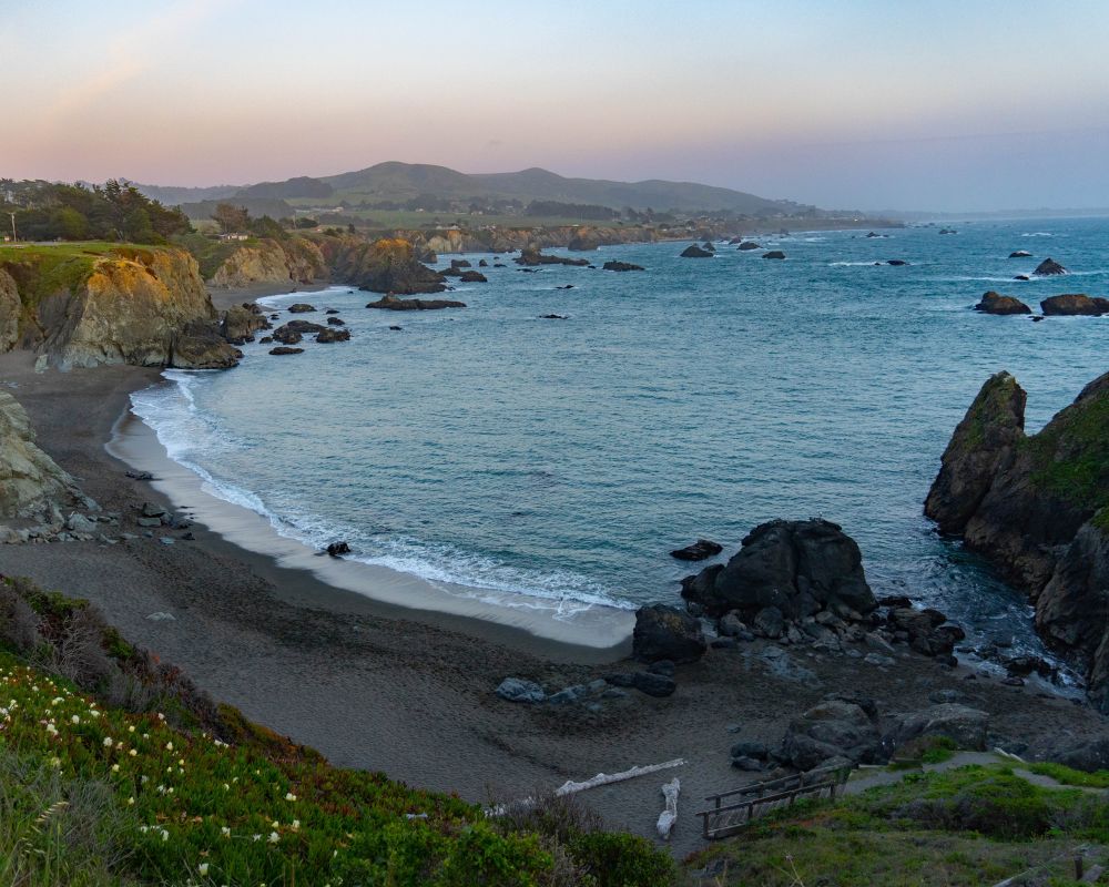 A view down on a curved beach framed by rocky outcroppings and the sea.