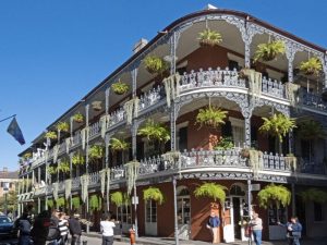 A corner building, 3 storeys, with lacy metal railings on balconies and plants hanging between each pillar.