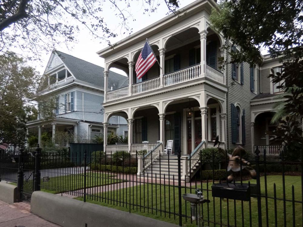 A free-standing home in the Garden District in New Orleans: 2 stories with wide porches and elegant pillars and railings.