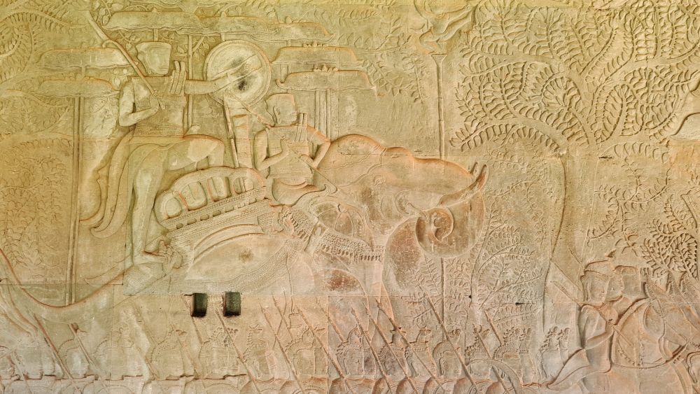 figures of a king on an elephant with marching solders below him.