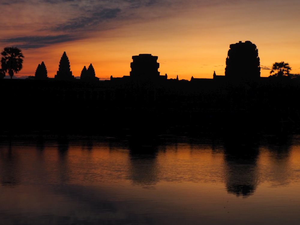 silhouettes of several temples against an orange sky, reflected in water in the foreground.