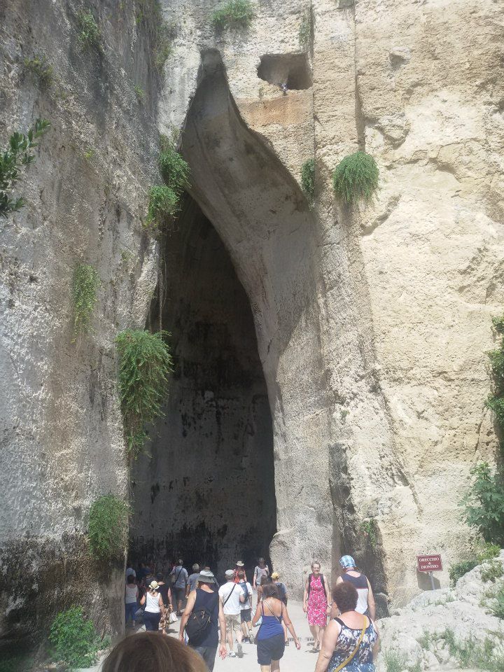 A large cave, very tall and narrow, with people looking very small below the entrance.