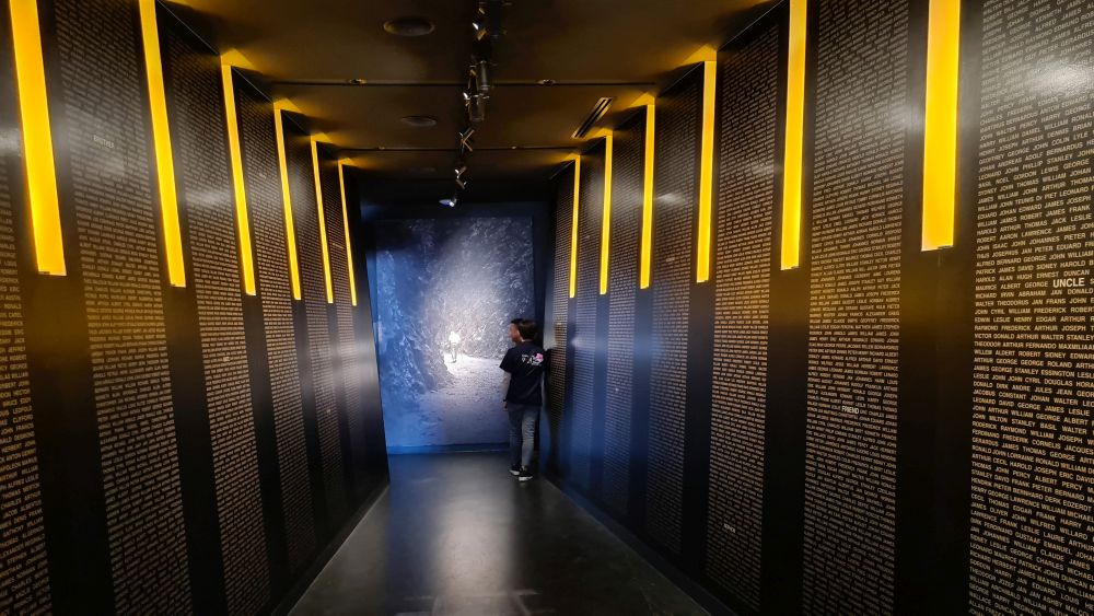 A dark hallway with indirect yellow vertical lights and between them, lots of names.