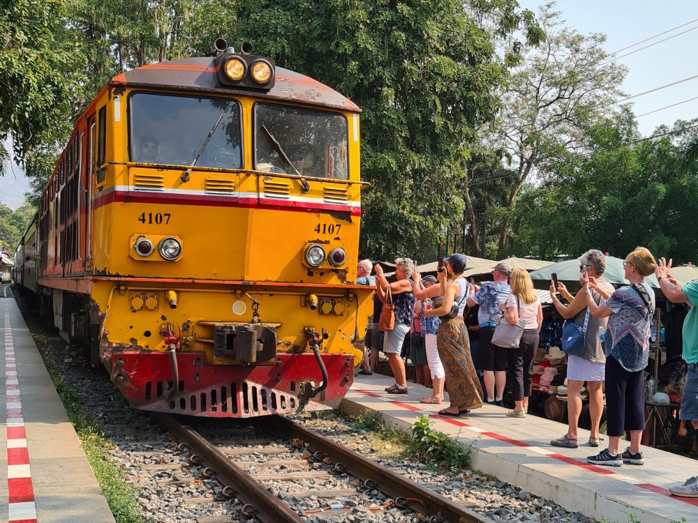 A yellow train locomotive, and a crowd of tourists on the platform next to it, taking pictures.