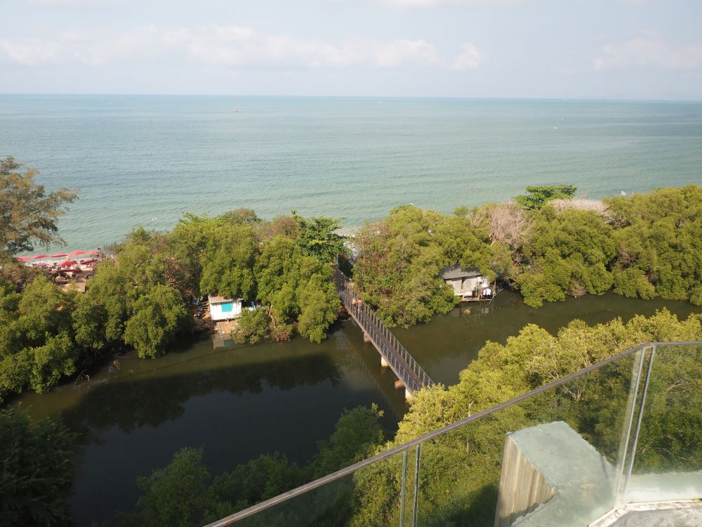 View from above of a river-like lagoon with a small bridge over it, greenery on both sides of it and the ocean beyond.