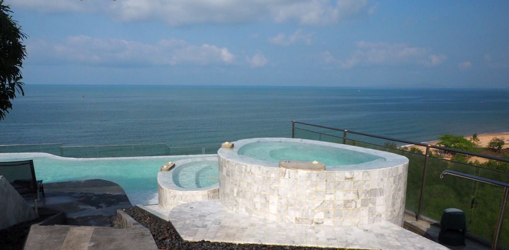 round or oval tubs with white tile on the outside, one higher than the other, the pool visible beyond and below them, and the sea beyond that.