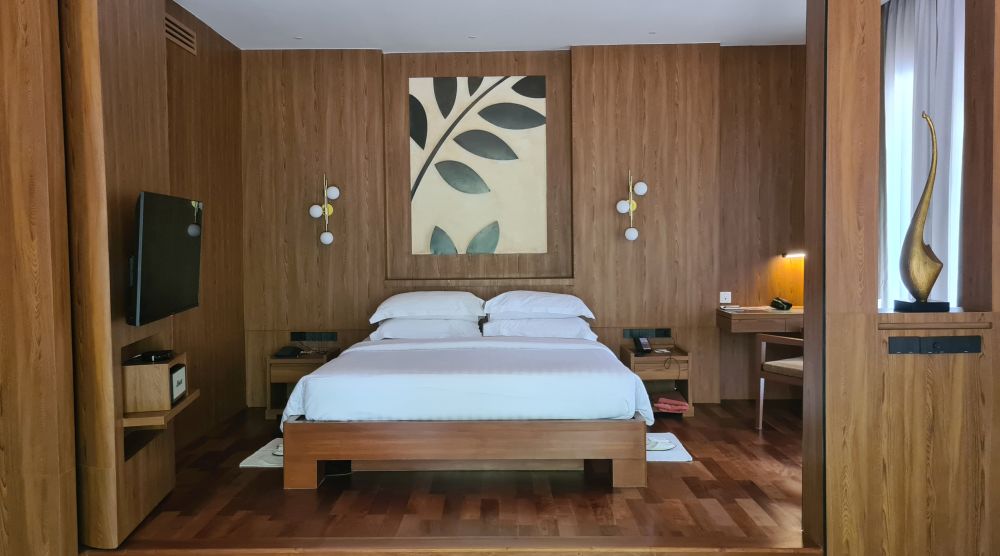 A large bed with white sheets and pillows, wood-panelled walls, an artwork above the bed with a leaf pattern, bedside tables on either side.