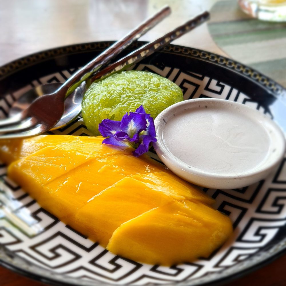 sliced mango, a ball of green sticky rice, and a bowl of white coconut sauce.