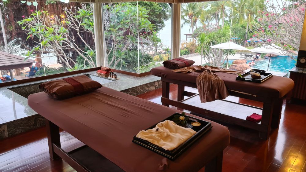 Two massage tables, with large windows on greenery and the pool.