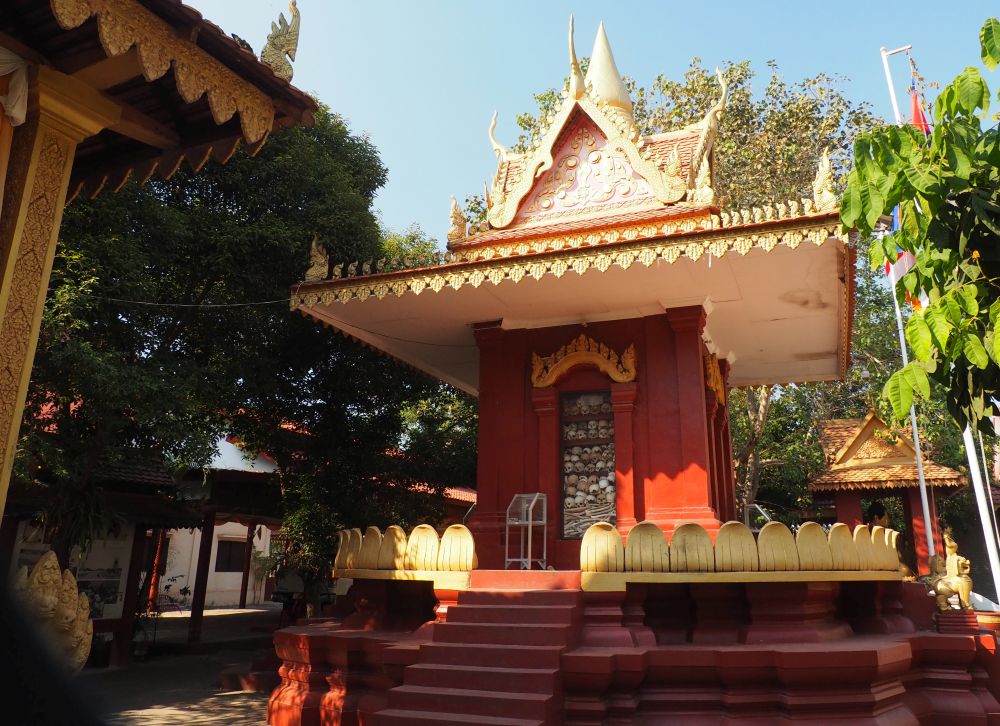 A small red shrine with traditional roof: a window shows a pile of skulls and other bones.