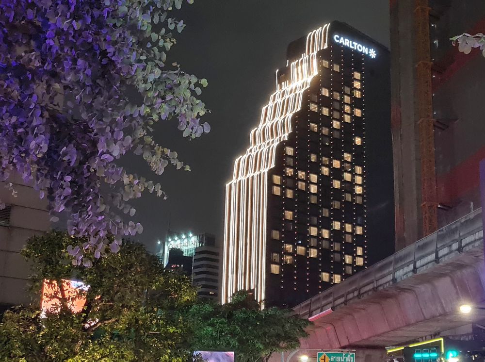 Night view looking up at the Carlton Hotel Bangkok Sukhumvit: vertical lines of white lights down the curves of its front like a waterfall.