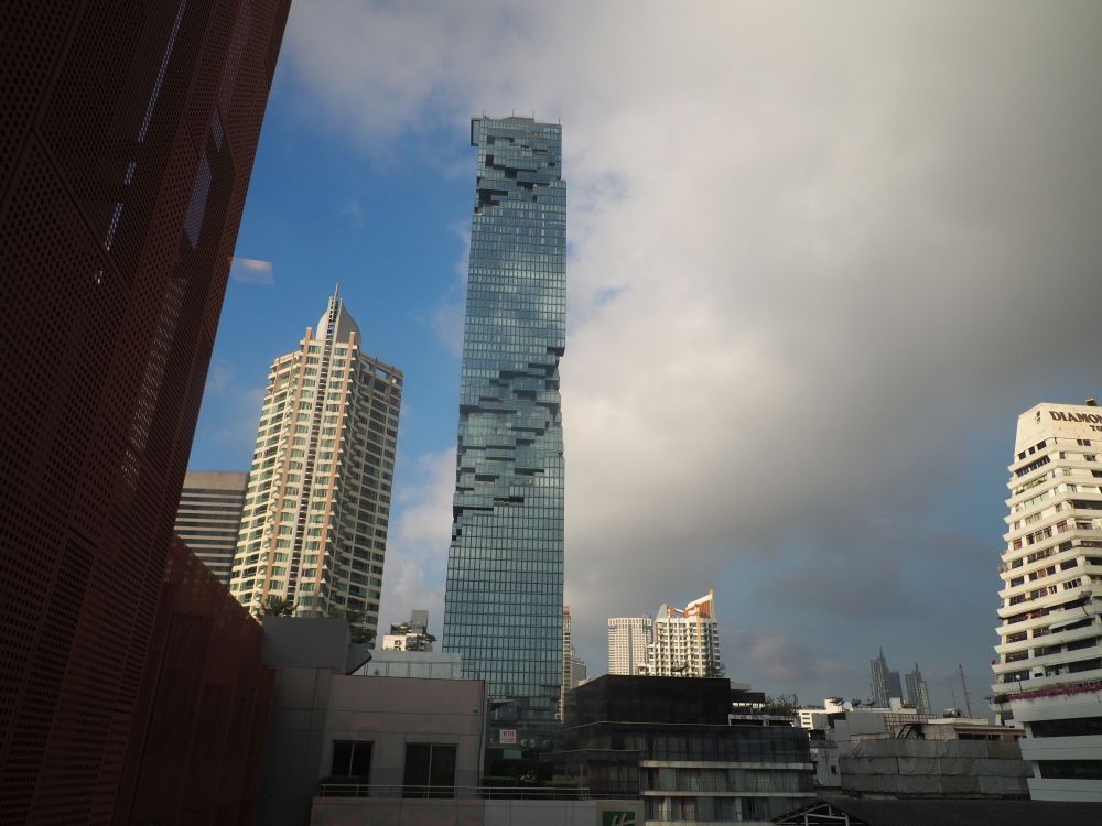 Several buildings but the one in the middle is tallest and shiny with glass, and some sort of cutout shapes here and there on its facade.