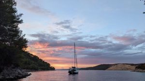 Anchored sailboat, sails down, in front of a pink post-sunset sky.