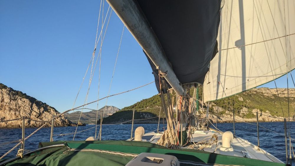 View from a sailboat under sail, looking forward with the edge of the sails visible overhead.