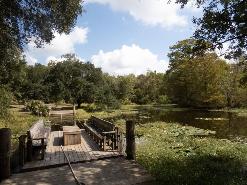 A small dock is a ferry landing on the edge of a small body of water at Vermilionville Historic Village.