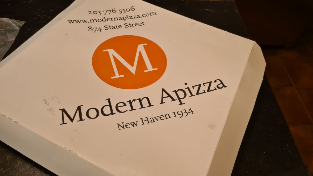 A pizza box with Modern Apizza's simple M logo and the words Modern Apizza New Haven 1934.