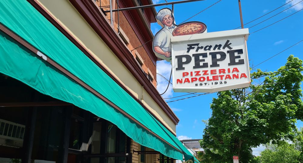 The sign on Pepe's reads: Frank Pepe's Pizzeria Napoletana Est. 1925 and pictures a chef holding a pizza.