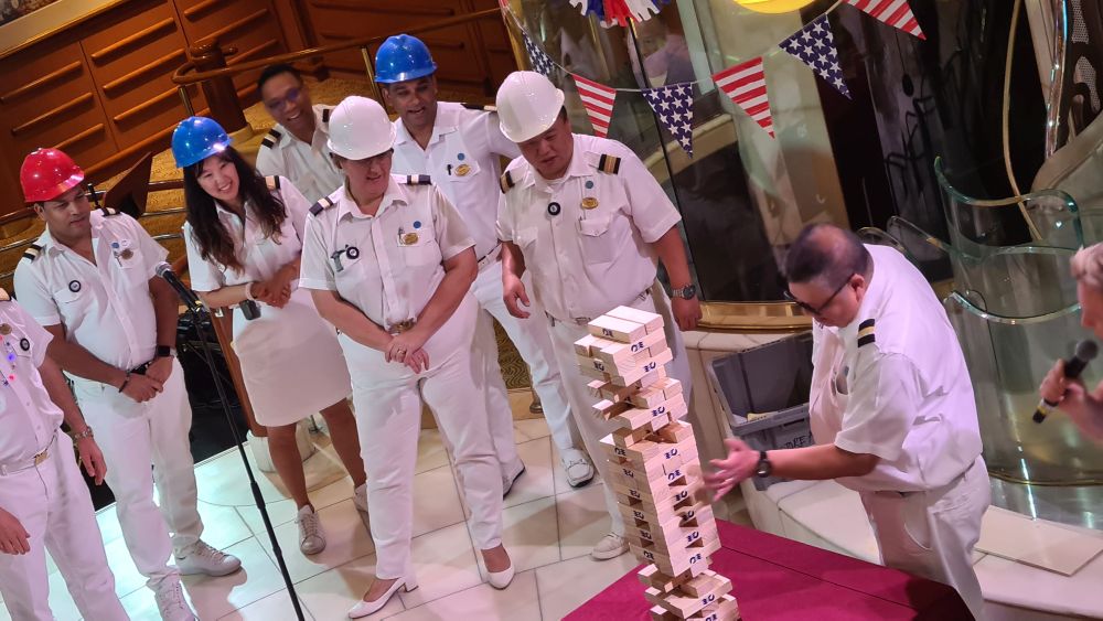 A group of Princess cruise crew in white uniforms and helmets. One is examining a Jenga tower.