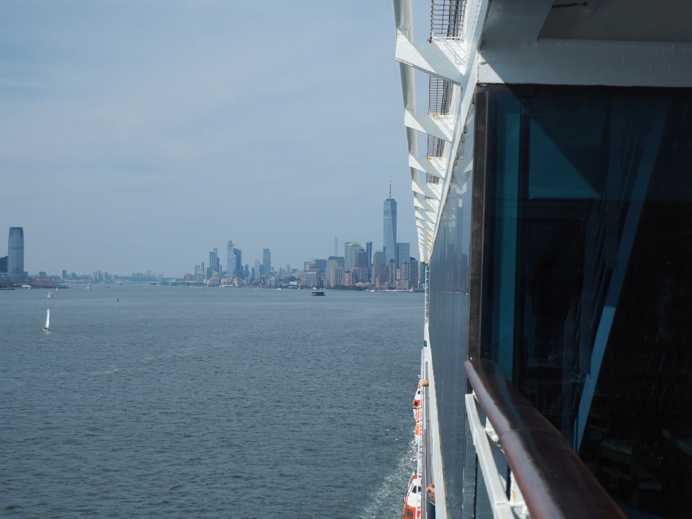 Sighting along the side of the ship, half of the New York City skyline is visible across the water behind the ship.