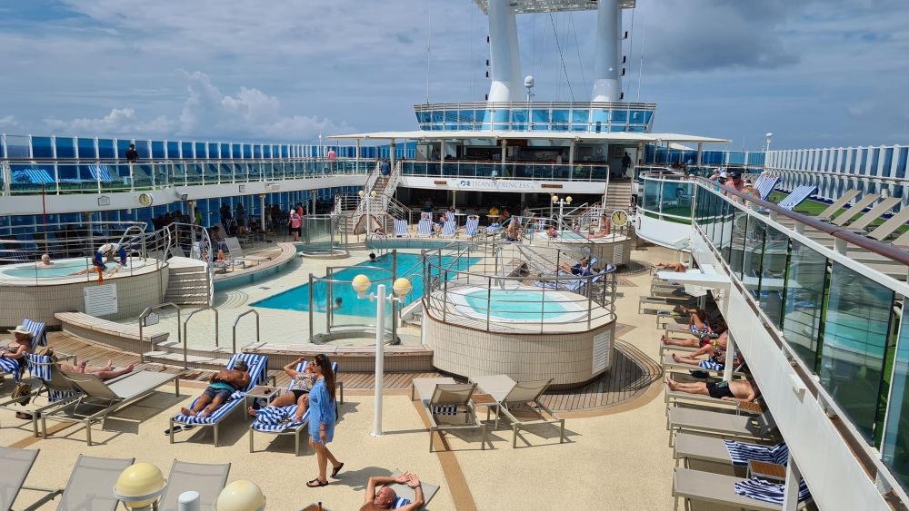 Looking at a pool from one deck up: rectangular, with round hot tubs around it and lots of lounge chairs.