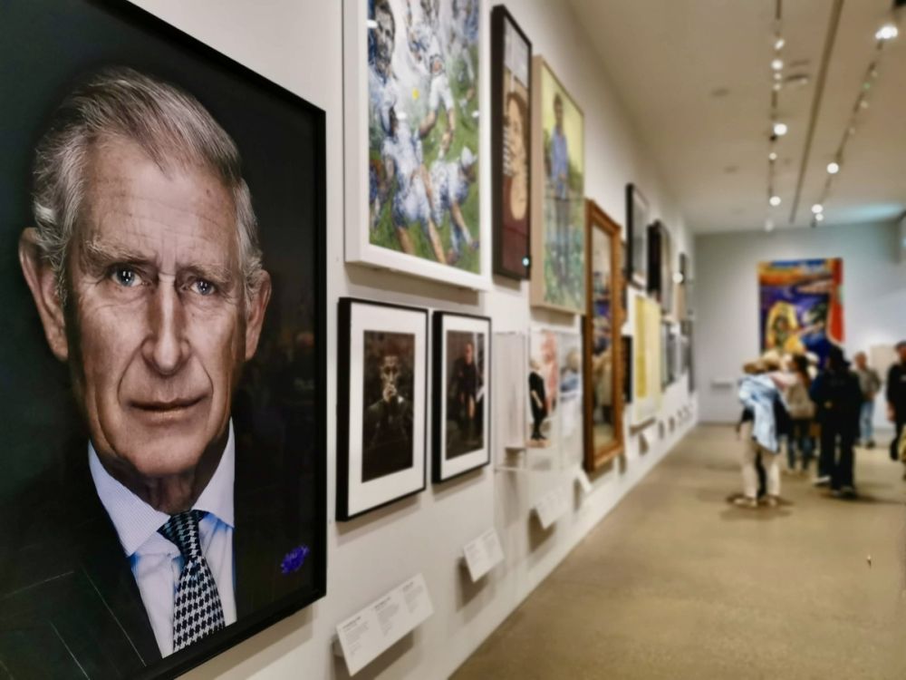 A wall of the gallery filled with paintings: the nearest is a portrait of King Charles.