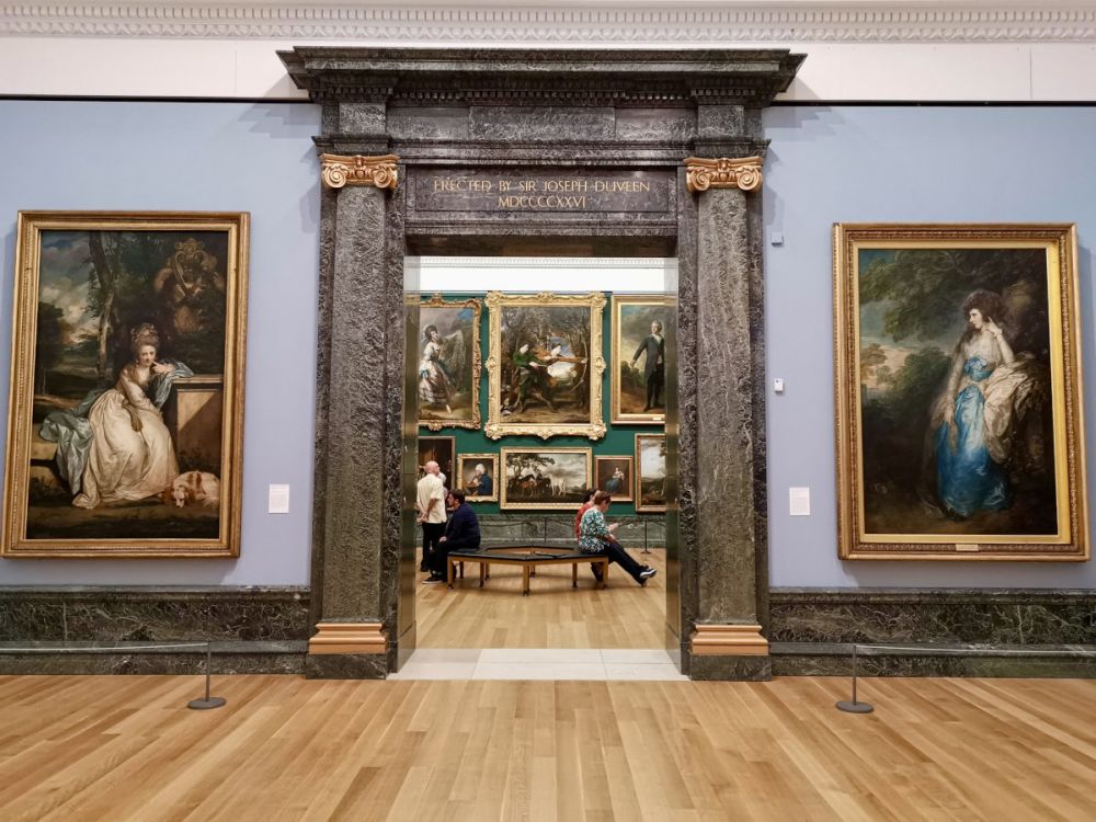 Looking from one gallery into the next through a monumental doorway: paintings on the wall either side of the doorway and also visible through the doorway on the far wall.