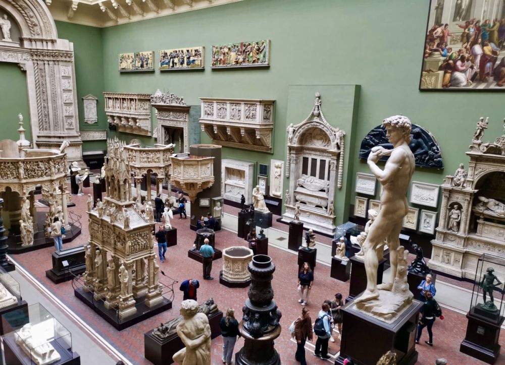 A view from above of a large room dotted with sculptures on the floors and walls, with some people between them.