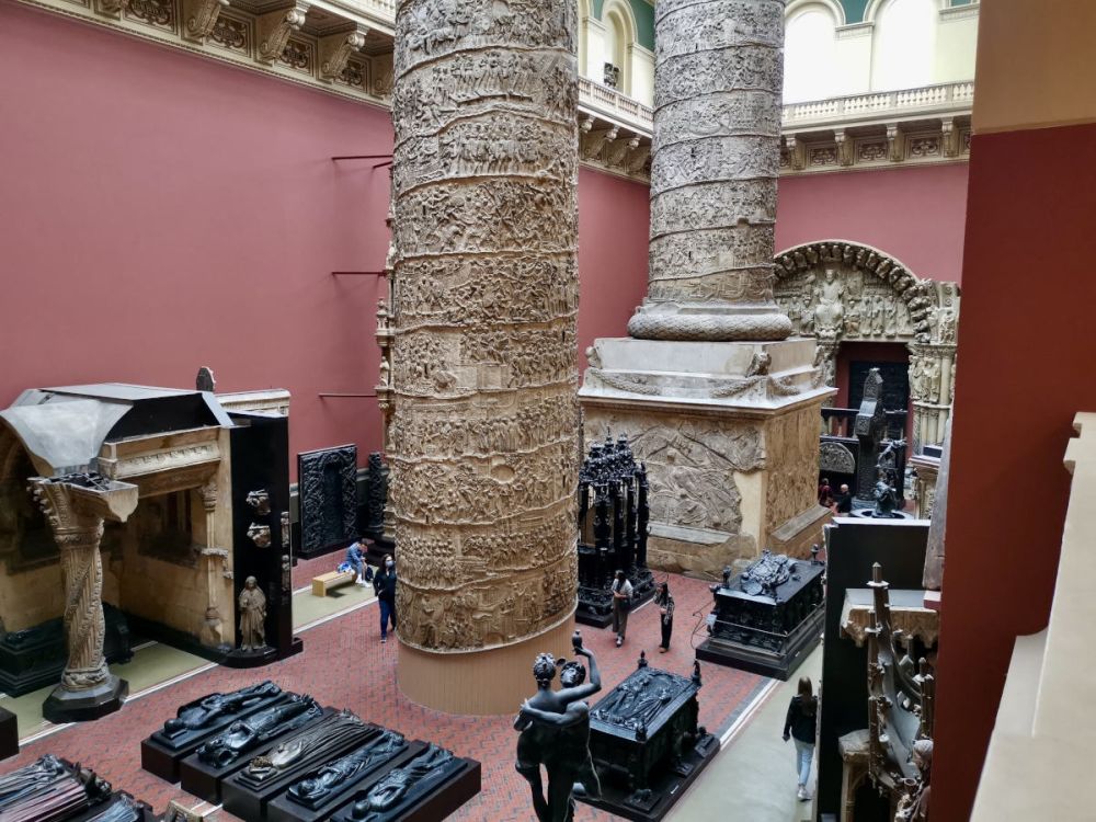 A view from above of a room in the museum, with two very tall and thick carved pillars on display.