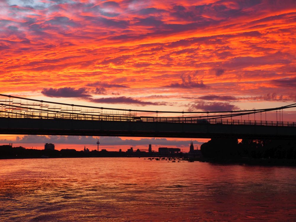 A brilliantly-colored sunset through clouds: bright orange and pink, reflected in the water.