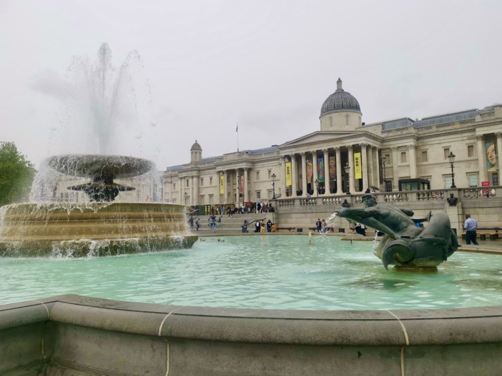 A large classical building with pillars across the front and a cupola on top with a fountain in front of it.