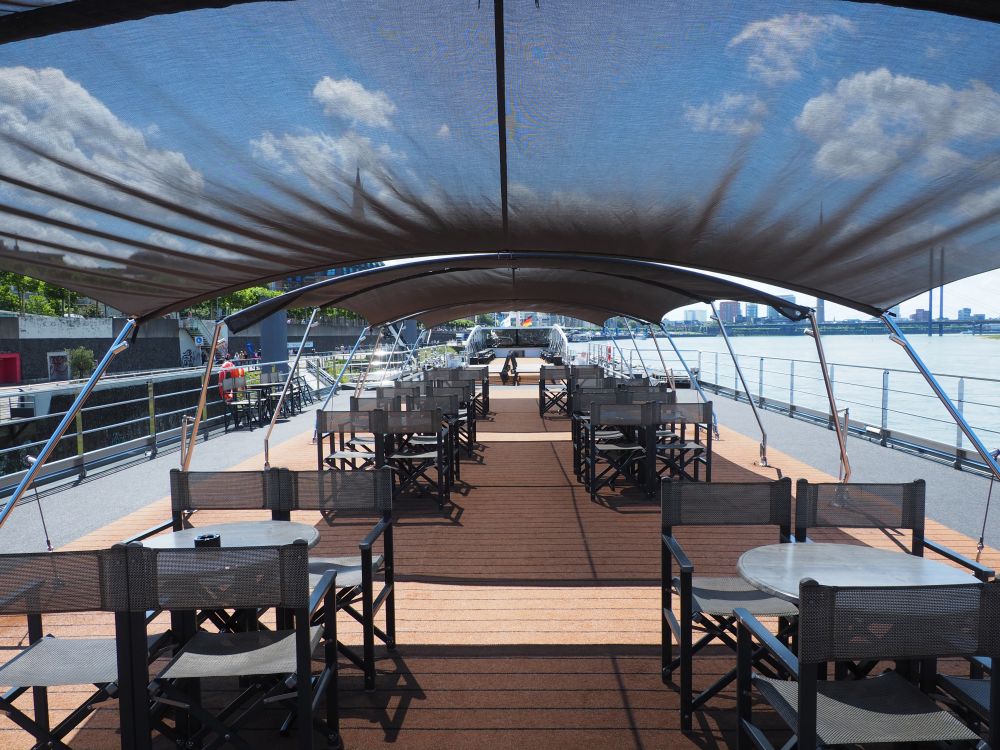 Looking down the length of the ship, chairs and tables in the foreground shaded by black cloths.