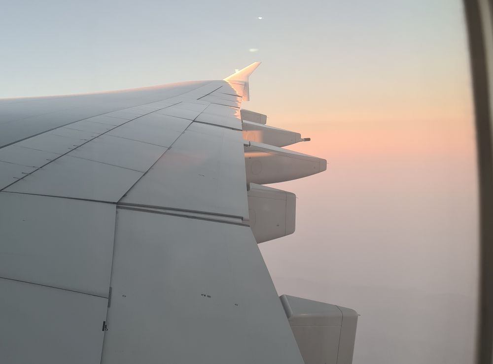 Looking out a window at an airplane wing and a pink sunrise sky.