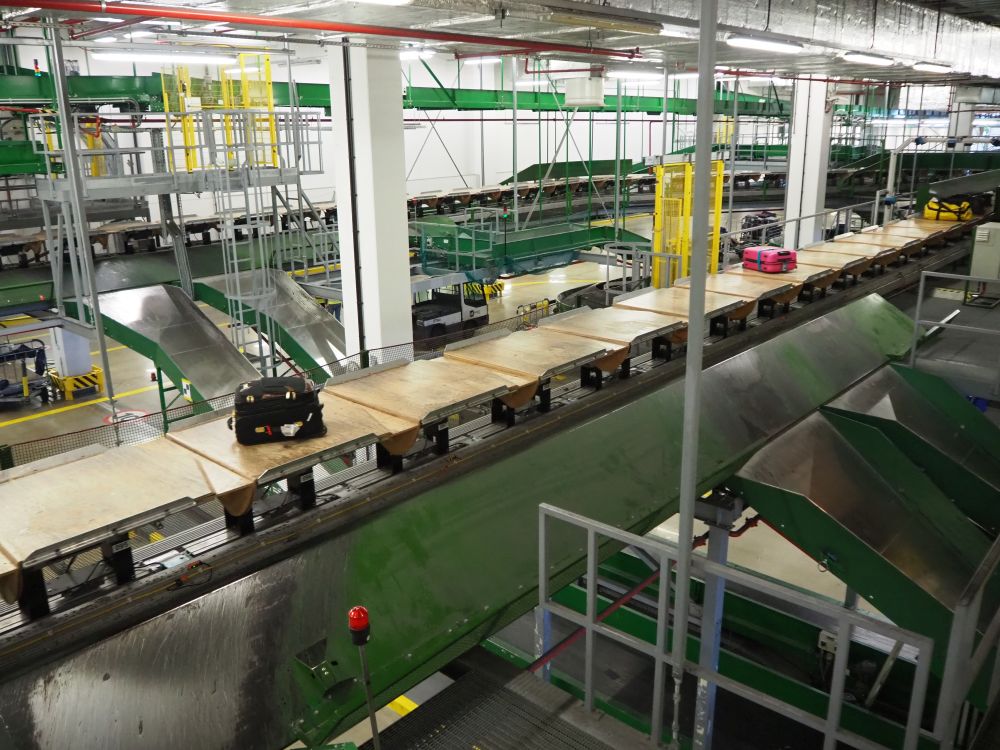 A large warehouse-like space with a conveyor belt carrying suitcases.