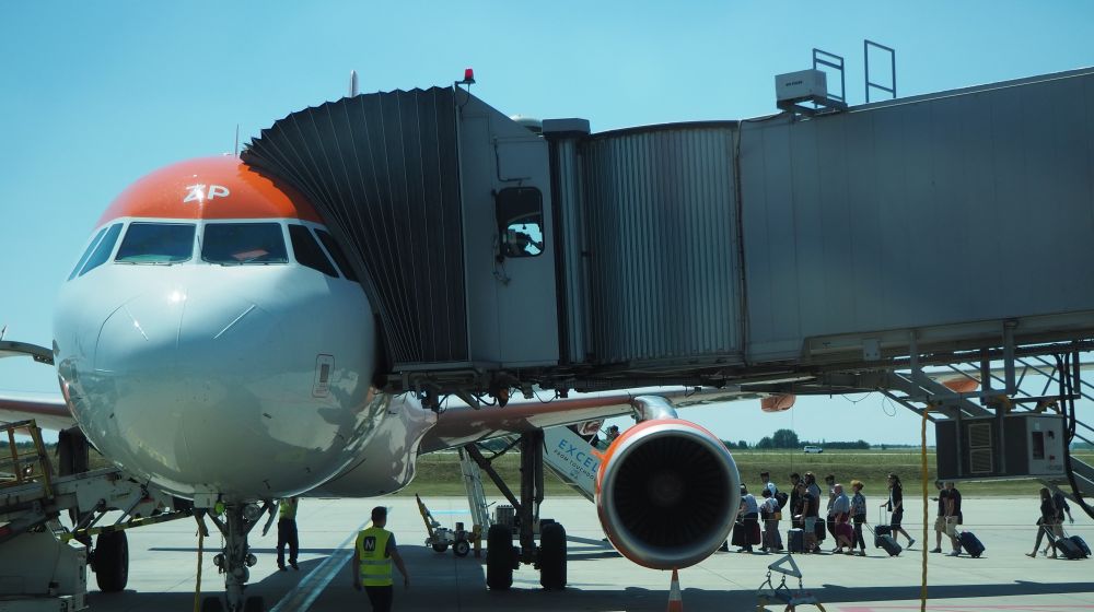 A plane parked with a walkway attached to it, but passengers walking upstairs to board the back end of the plane.