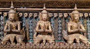 Three gold-painted figures of buddha holding their hands together as if in prayer.