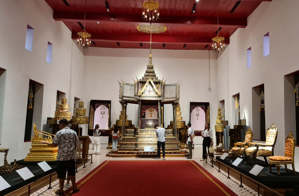 A large high-ceilinged room with a large throne at the end and smaller ones along the two sides.