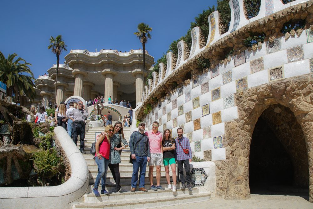 People pose at the bottom of a stairway next to a colorfully tiled, curved wall.