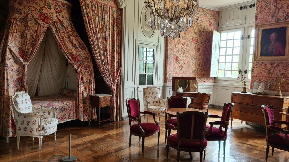 A bed in an alcove with a canopy, assorted chairs and tables around the room.