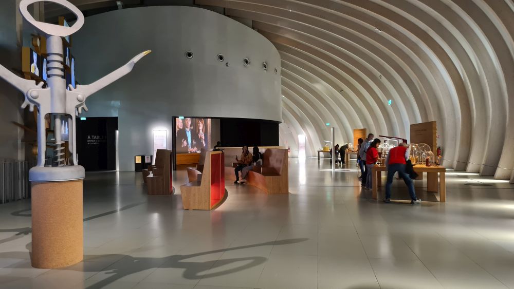 A large space with a high curved roof, a huge corkscrew on the left and people looking at a display on the right.