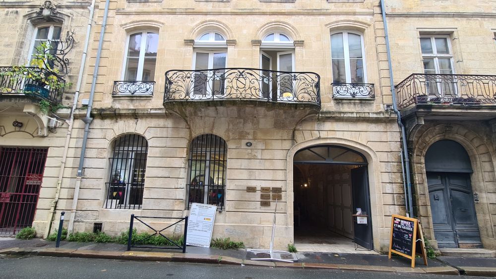 A white stone building with arched windows and a decorative iron balcony above the ground floor.