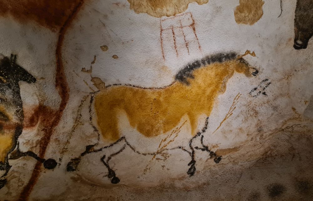 A horse painted onto a rough rock surface. It is brown on its back and sides and white underneath, with a black mane.