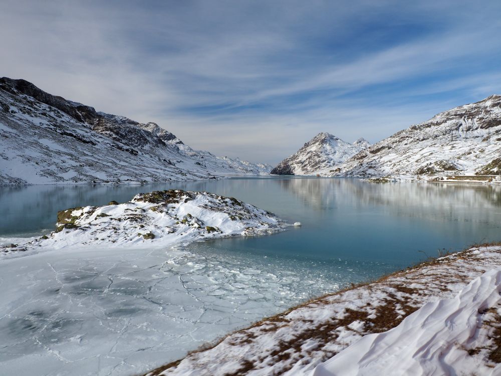 A body of water, iced over and surrounding by snow-covered hills.